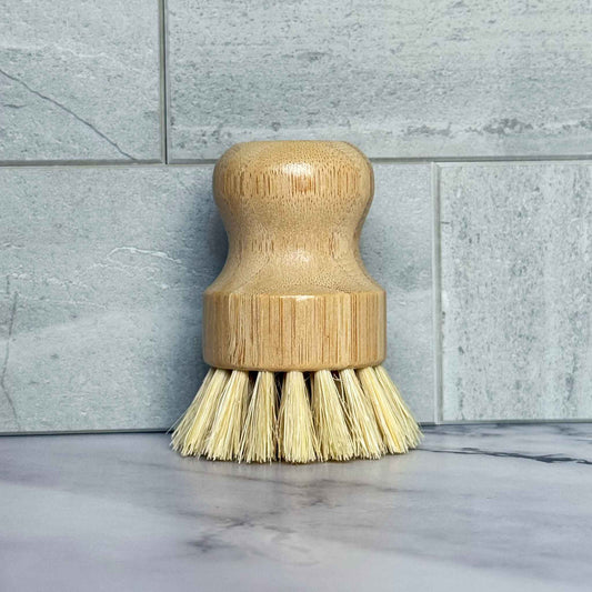 Bamboo dish brush with sisal bristles on a marble surface with tiled wall background