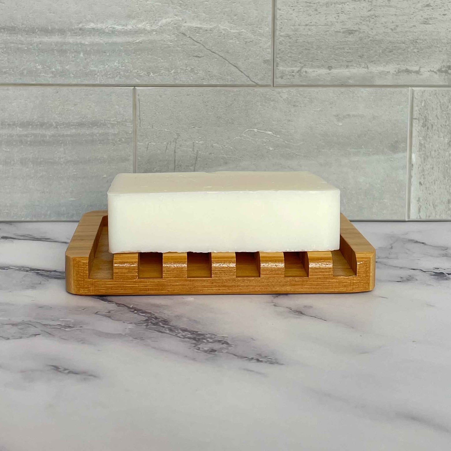 Bar of soap on a bamboo soap dish with a marble and tile background