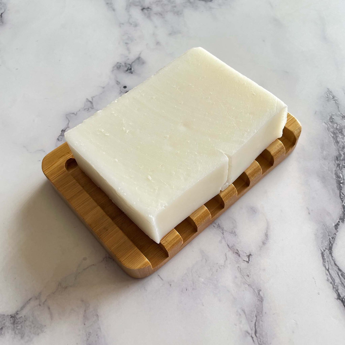 Bar of soap on a bamboo soap dish against a marble background
