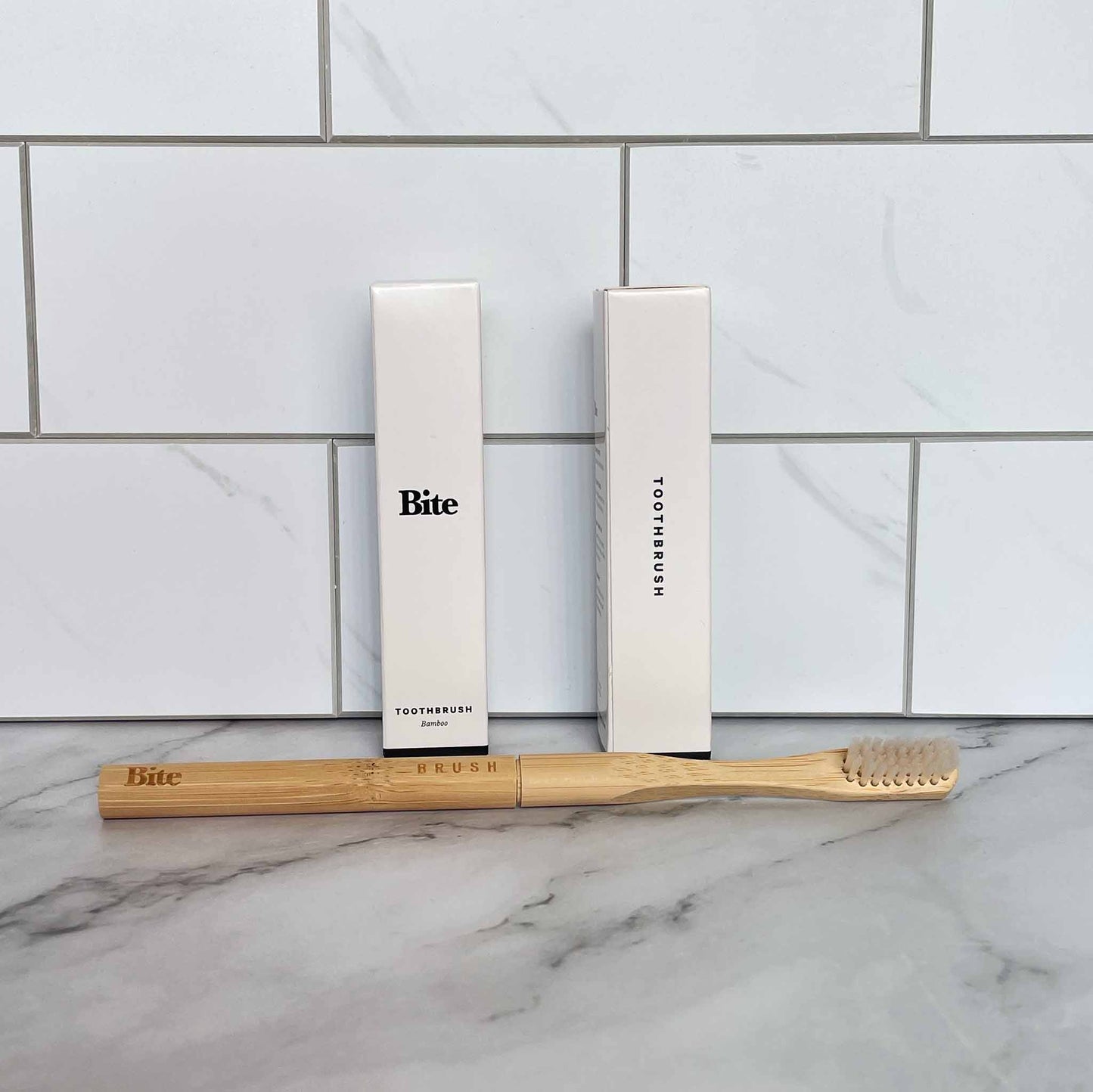 Bamboo toothbrush and packaging with 'Bite' branding on a marble surface.