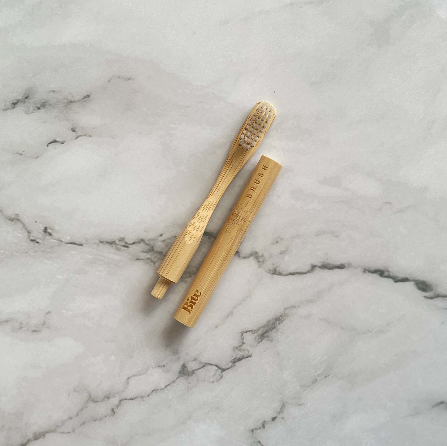 Bamboo toothbrush, detachable head next to holder, on a marble surface