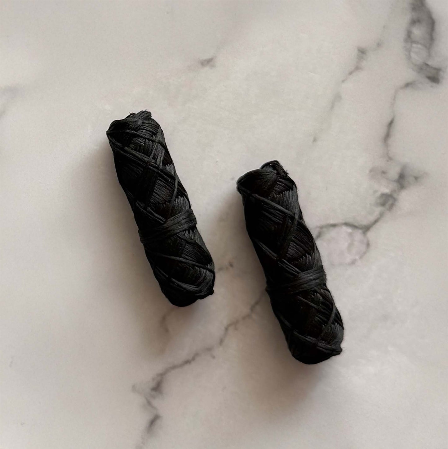Two charcoal dental floss refill rolled on a marble surface