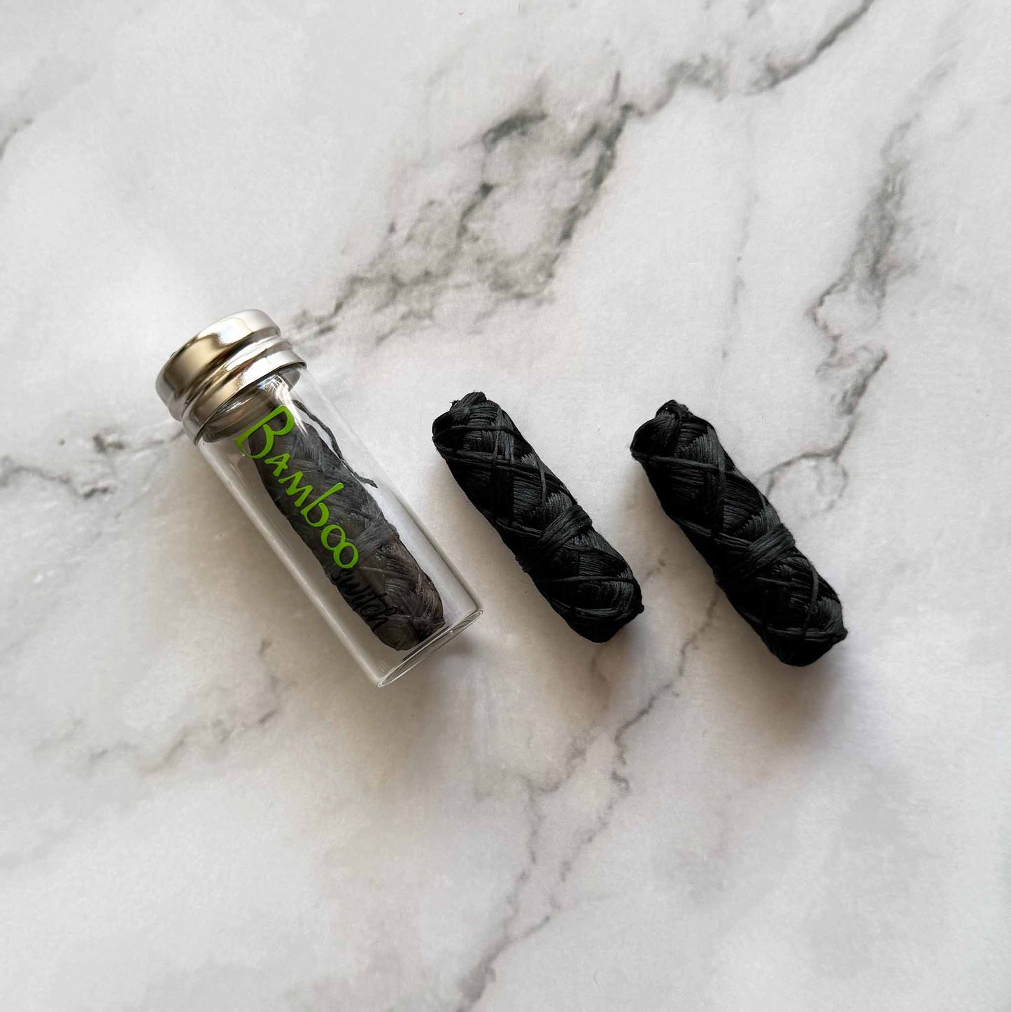 Charcoal bamboo dental floss black sticks and one in a clear container on a marble surface