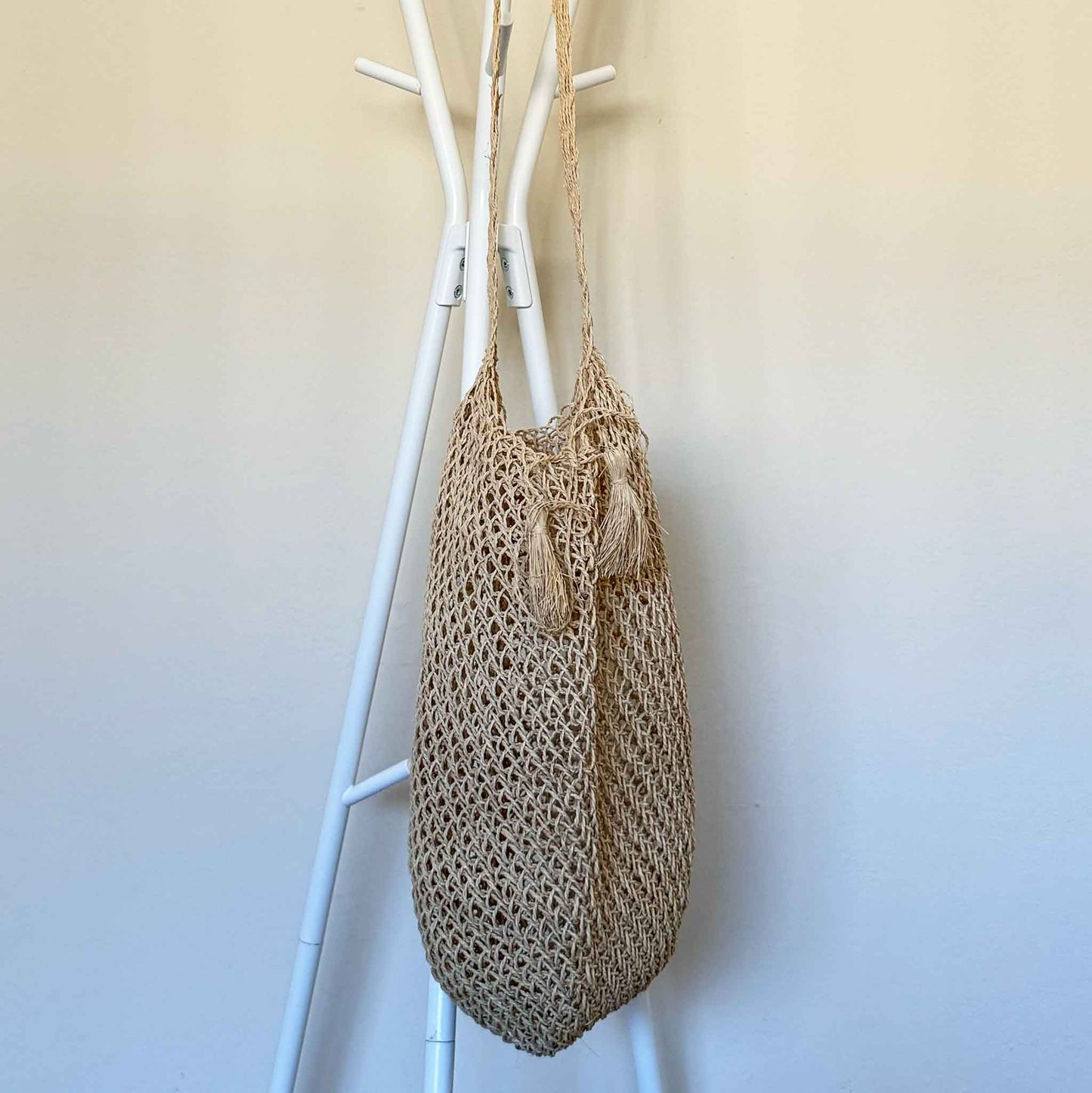 Handwoven Cumare Fiber Mochila with a strap hanging on a white coat rack against a light background