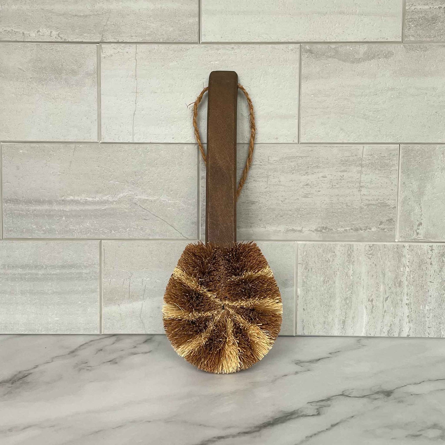 Brown brush with a wood handle on a marble surface with a tiled wall background