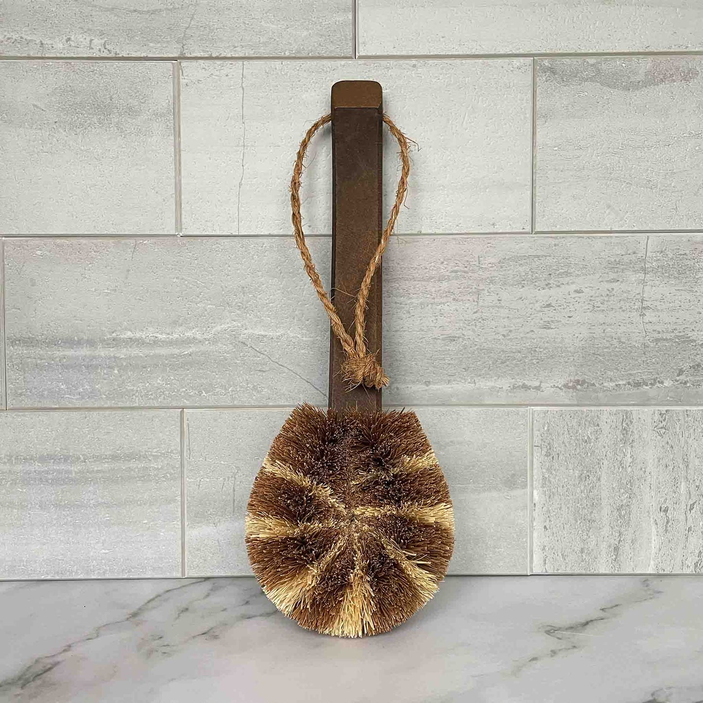 Bristle brush with a wooden handle on a marble surface with a tiled wall background