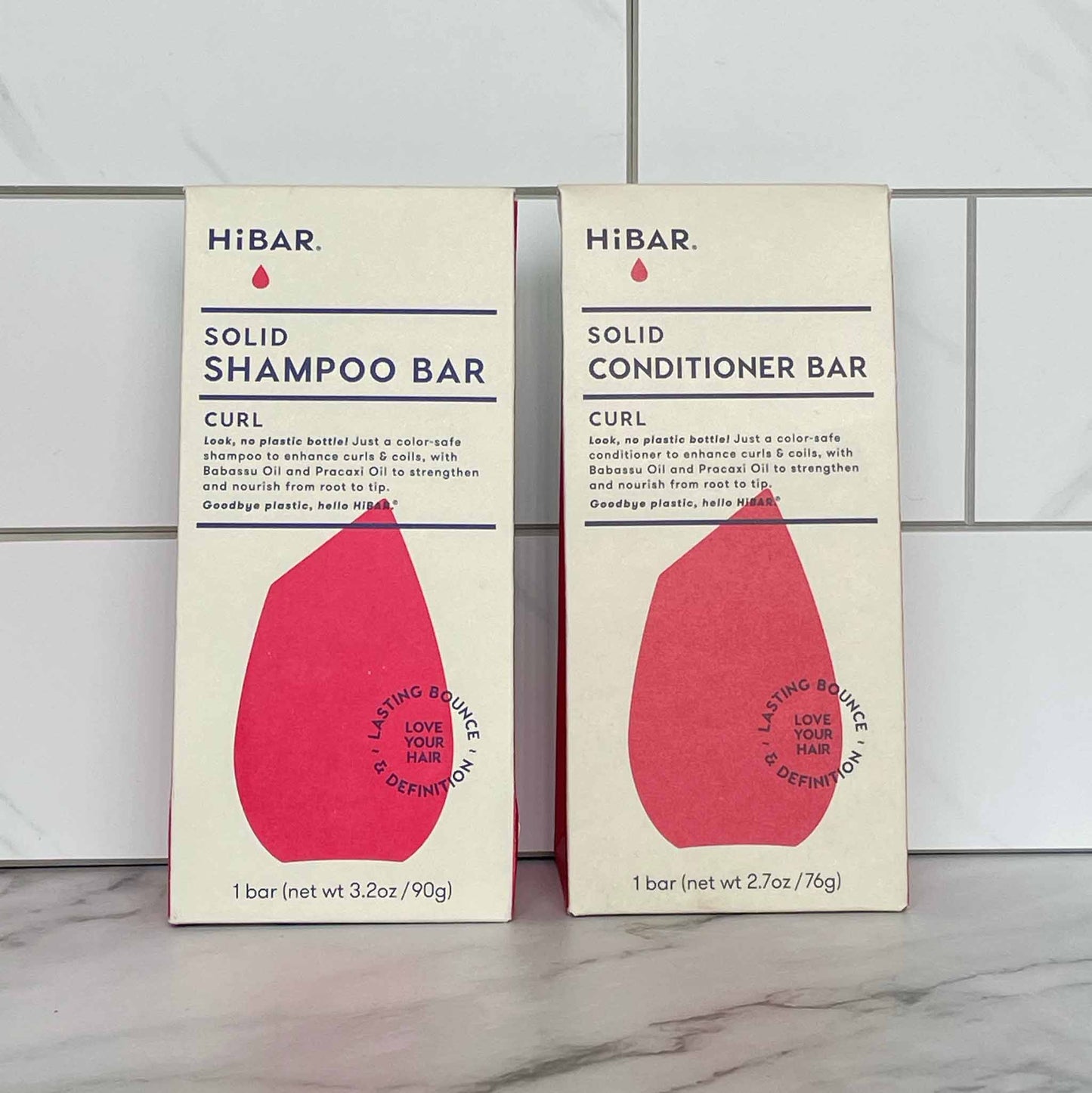 Two boxes of HIBAR Curl solid shampoo and conditioner bars on a tiled wall background