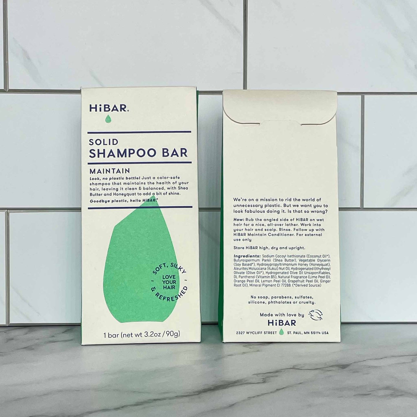 Two HIBAR Maintain solid shampoo bar packages on a tiled bathroom floor.