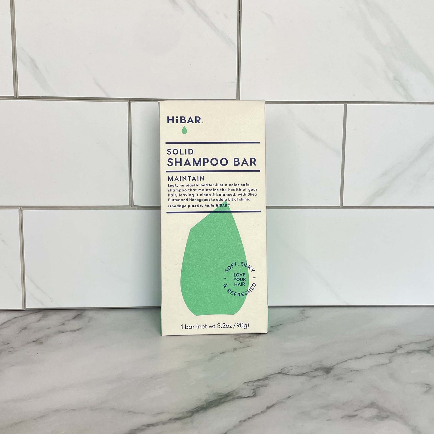 HiBar Maintain solid shampoo bar packaging on a marble surface with tiled wall background