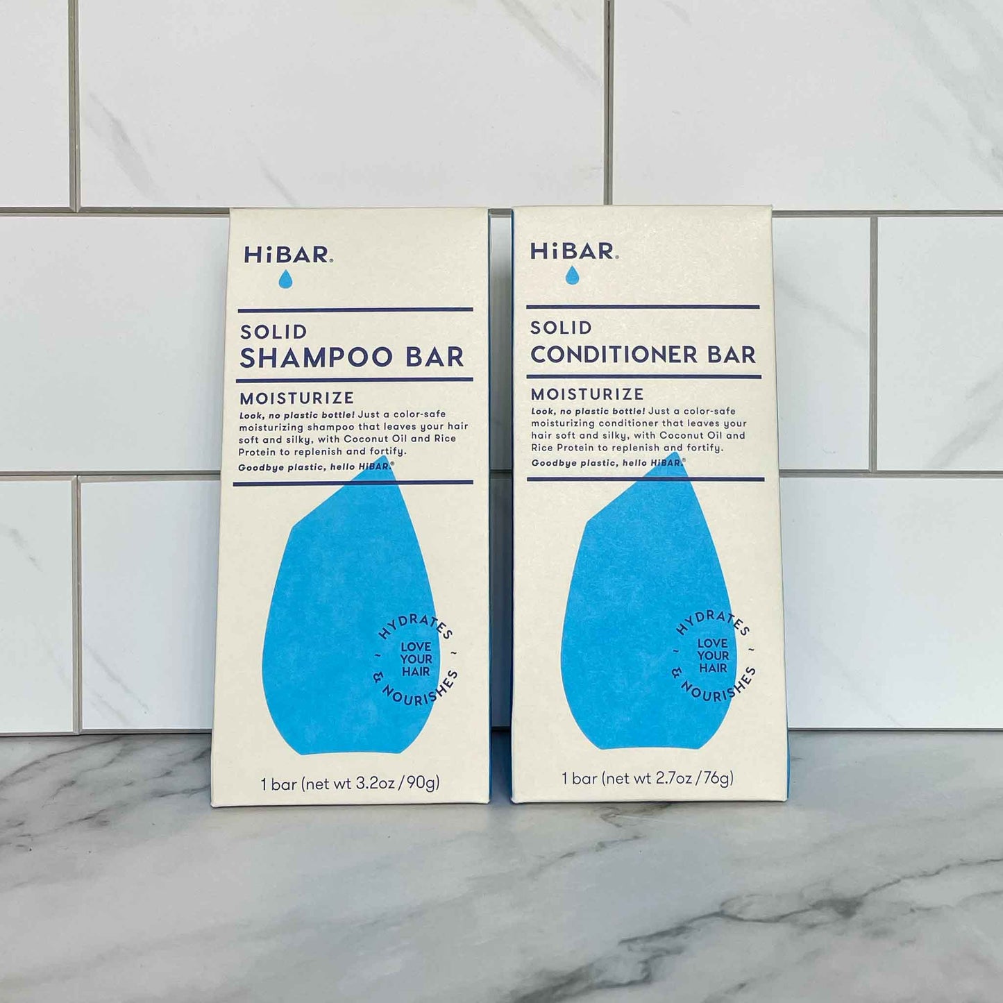 Two HiBAR Moisturize solid shampoo and conditioner bar packages on a tiled bathroom wall.