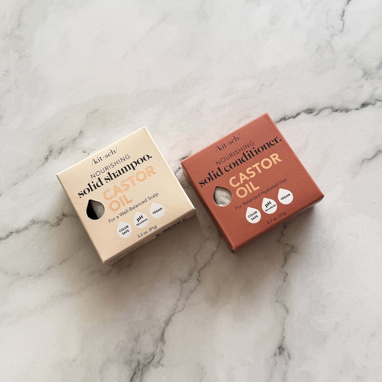 Two boxes of Kitsch solid castor oil shampoo and conditioner on a marble surface