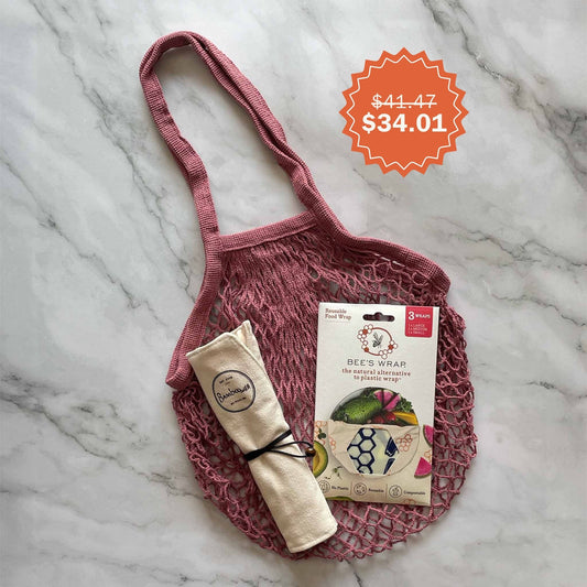 Set of bamboo utensils in a cotton pouch with a blush mesh bag and beeswax wrap box on a marble surface