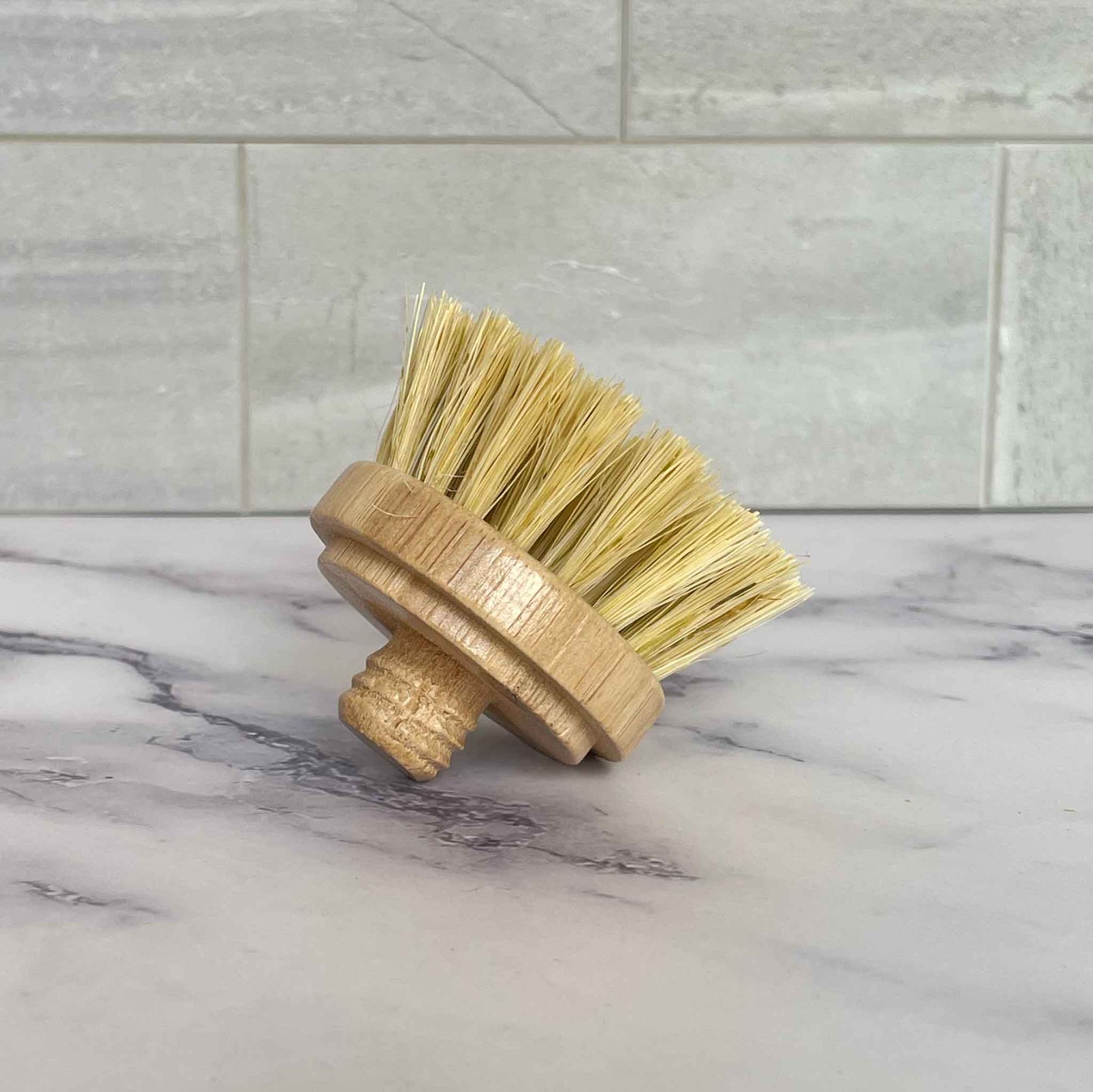 Bristle brush with bamboo handle on a marble surface with tiled wall background
