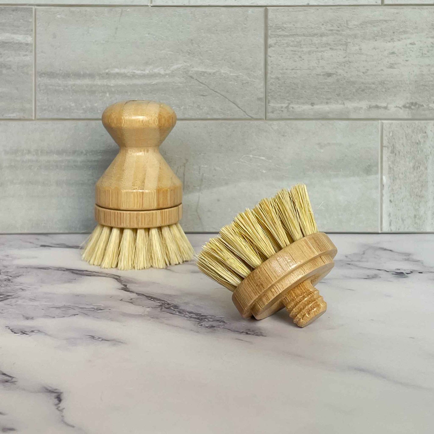 Two bamboo dish brushes on a marble surface with a tiled wall background