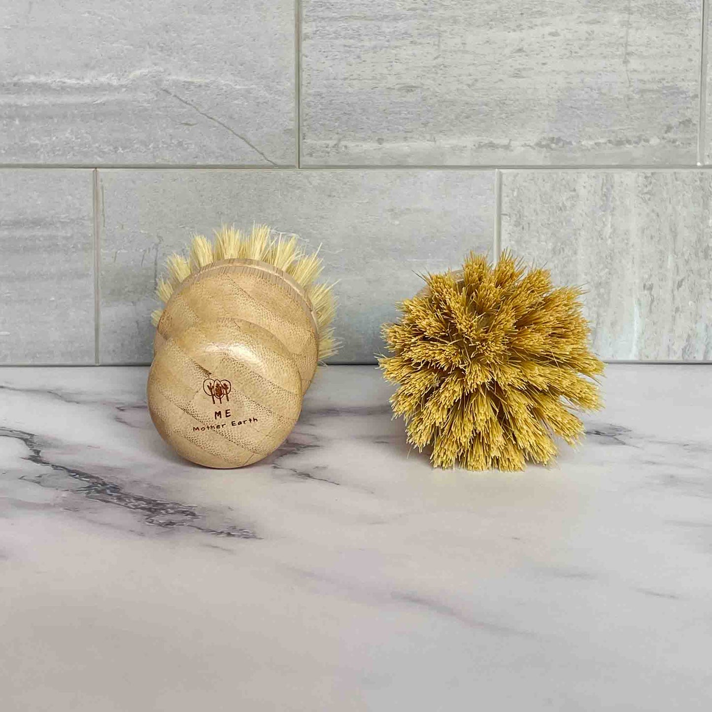Bamboo brushes with sisal bristles on a marble surface with tiled wall background.