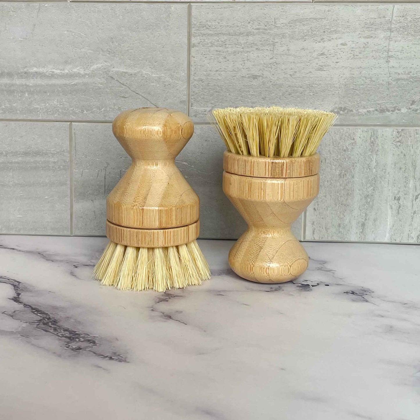 Two bamboo sisal dish brushes with bristle heads on a marble surface.