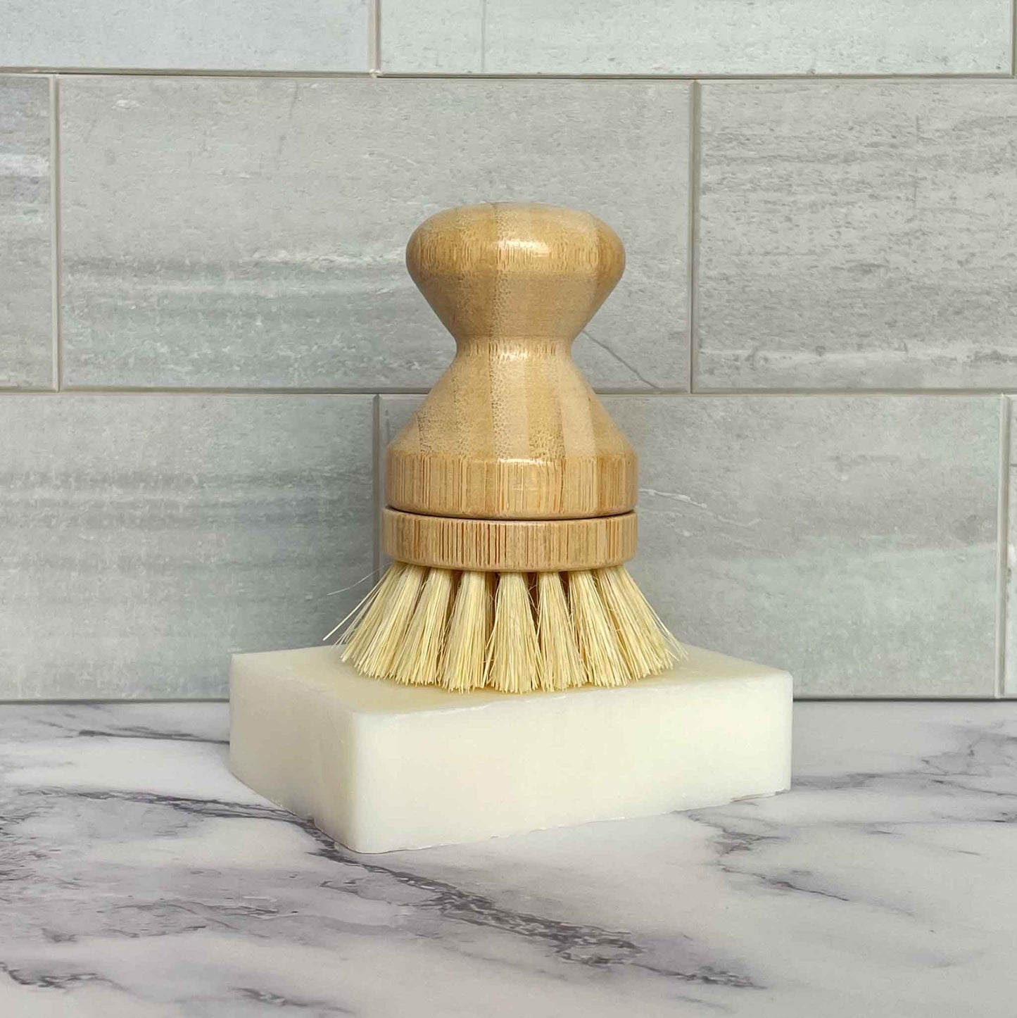 Bamboo dish brush with bristles on a dish soap bar against a tiled wall background