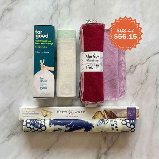 Collection of eco-friendly products including beeswax wraps roll, unpaper towels and compostable kitchen trash bags on a marble surface.