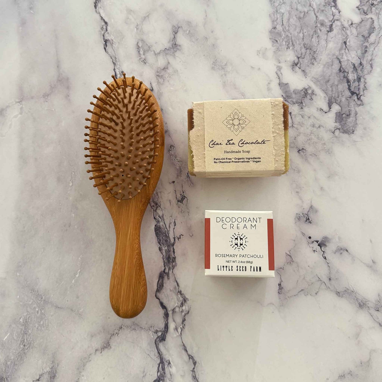 Bamboo hairbrush, soap bar, and deodorant cream on a marble surface