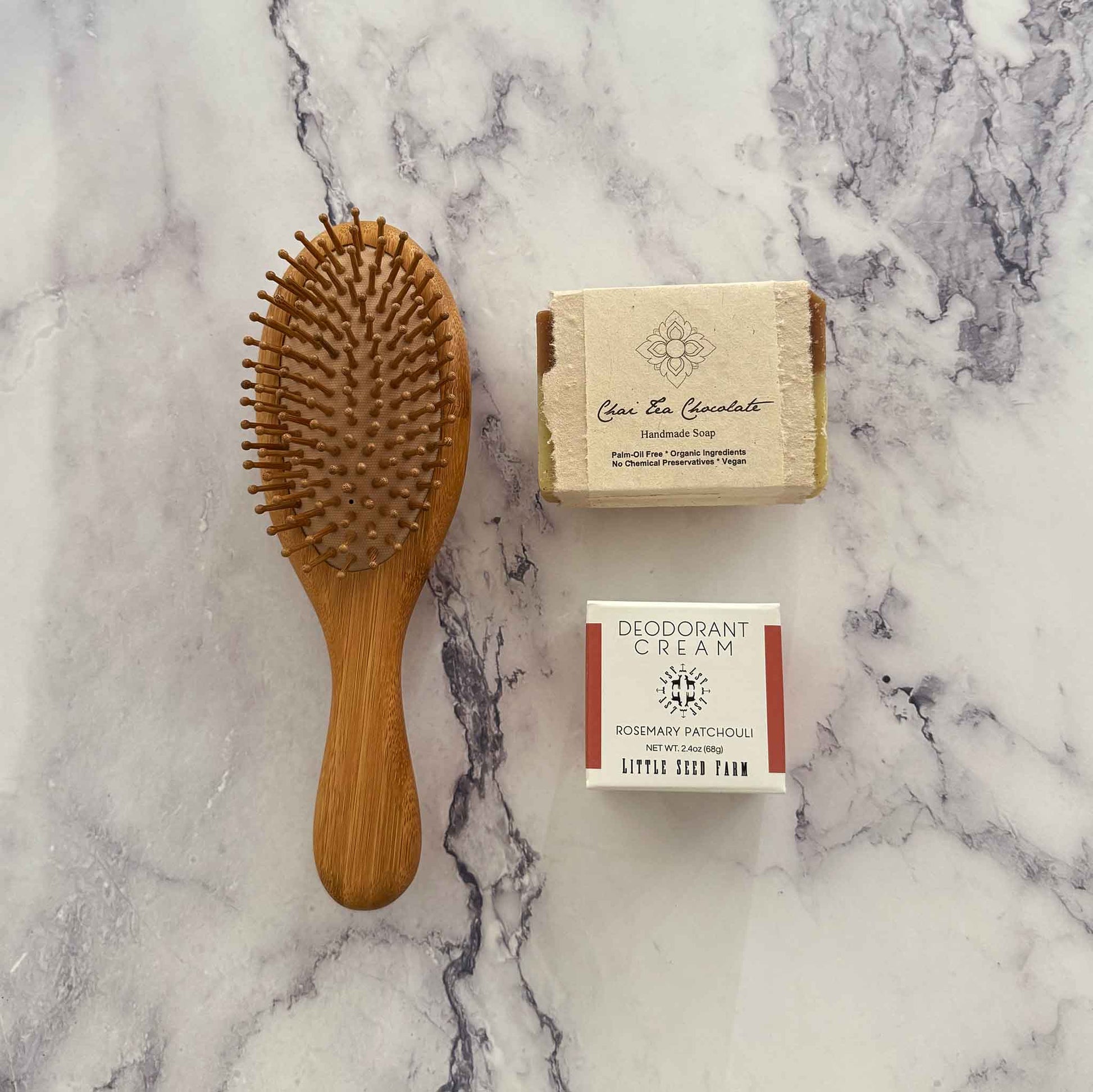 Bamboo hairbrush, soap bar, and deodorant cream on a marble surface