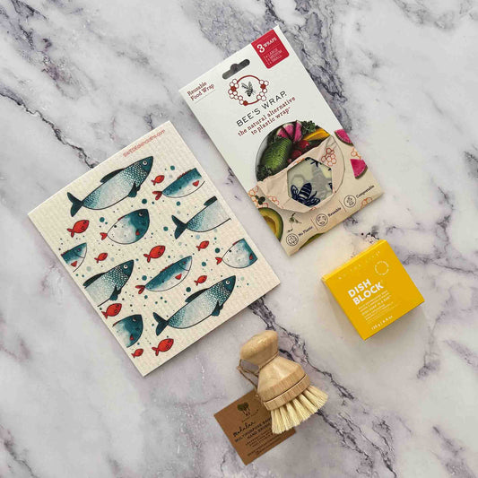 Set of eco-friendly cleaning products including a scrubber, dish block, Swedish dishcloth and Beeswax Food Wrap on a marble surface.