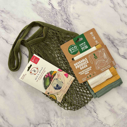 Green reusable mesh bag, beeswax food wrap, cello product bag set on a marble surface