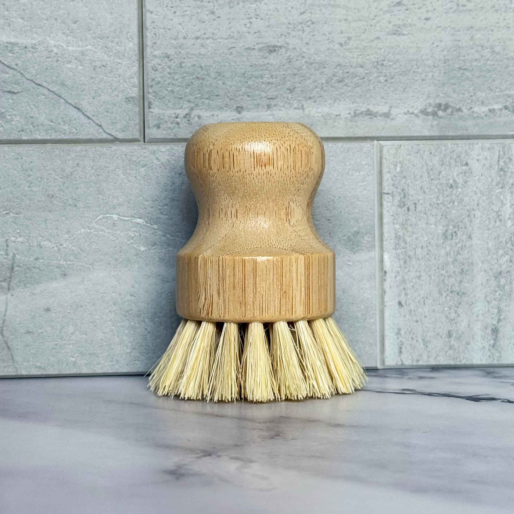 Bamboo dish brush with sisal bristles on a marble surface with tiled wall background