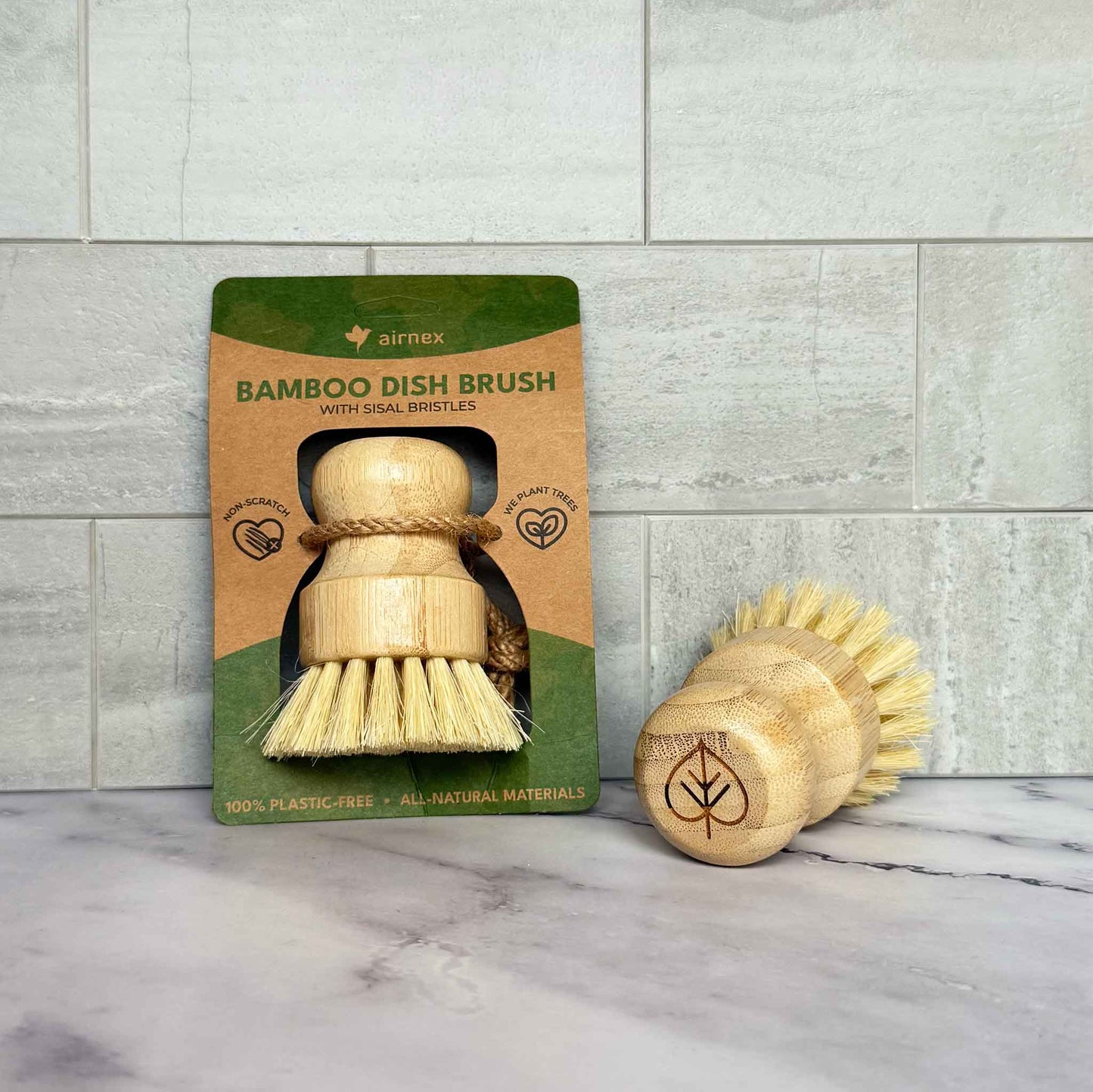 Bamboo dish brush with packaging on a marble surface and tiled wall background