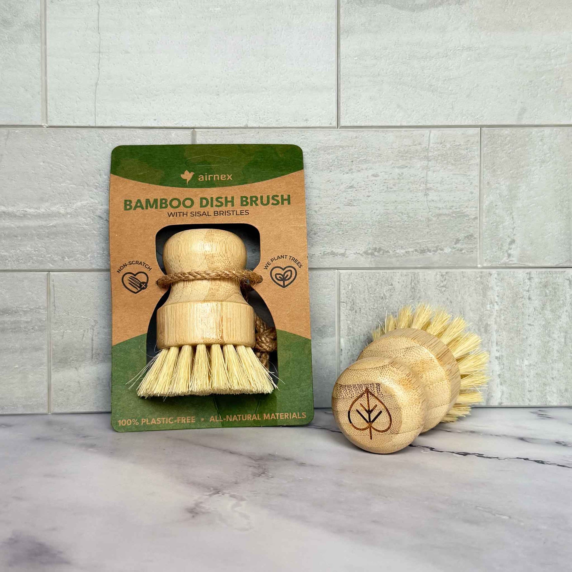 Bamboo dish brush with packaging on a marble surface and tiled wall background