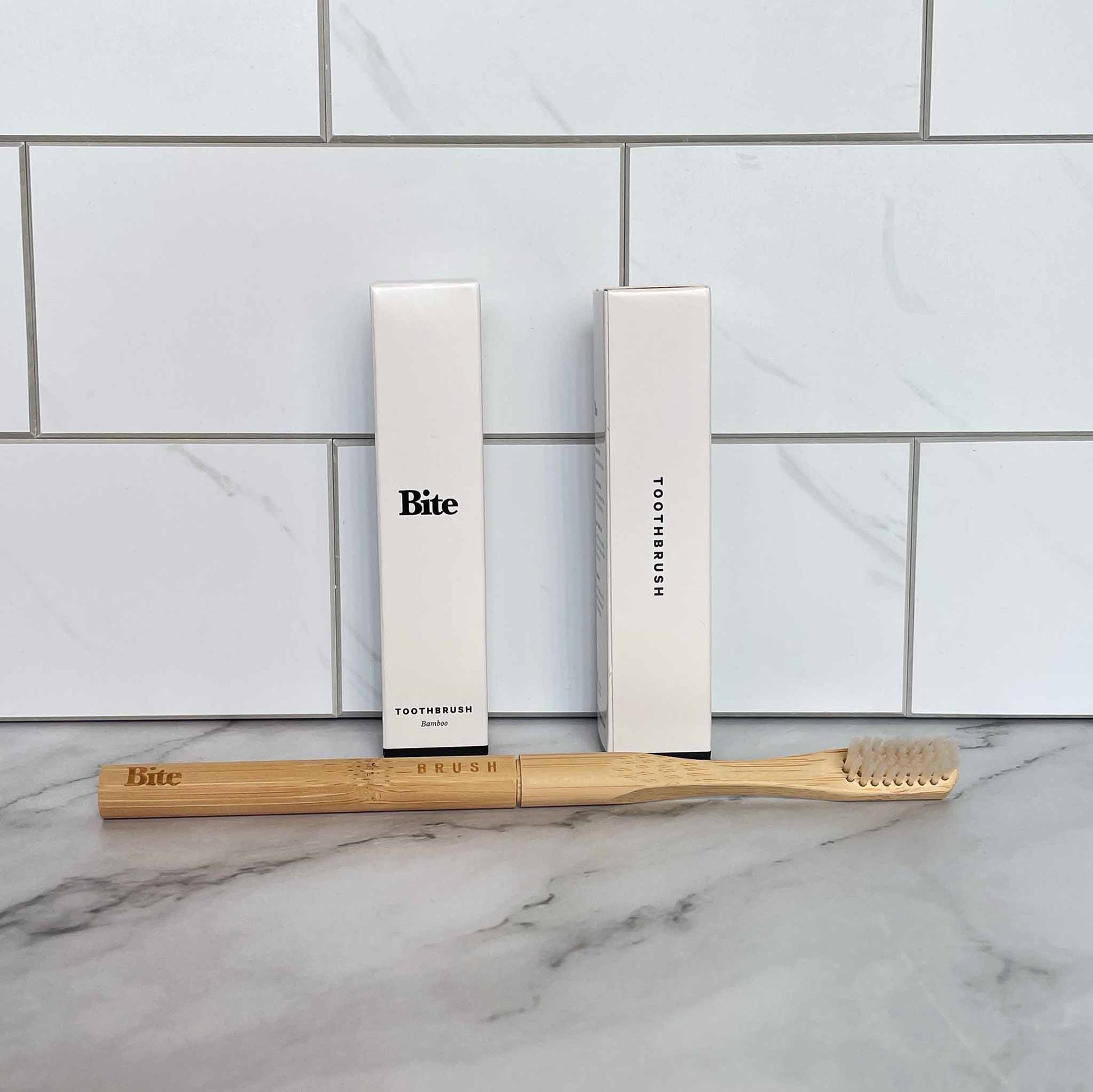 Bamboo toothbrush and packaging with 'Bite' branding on a marble surface.