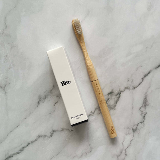 Bamboo toothbrush and its packaging on a marble surface, branded 'Bite'.