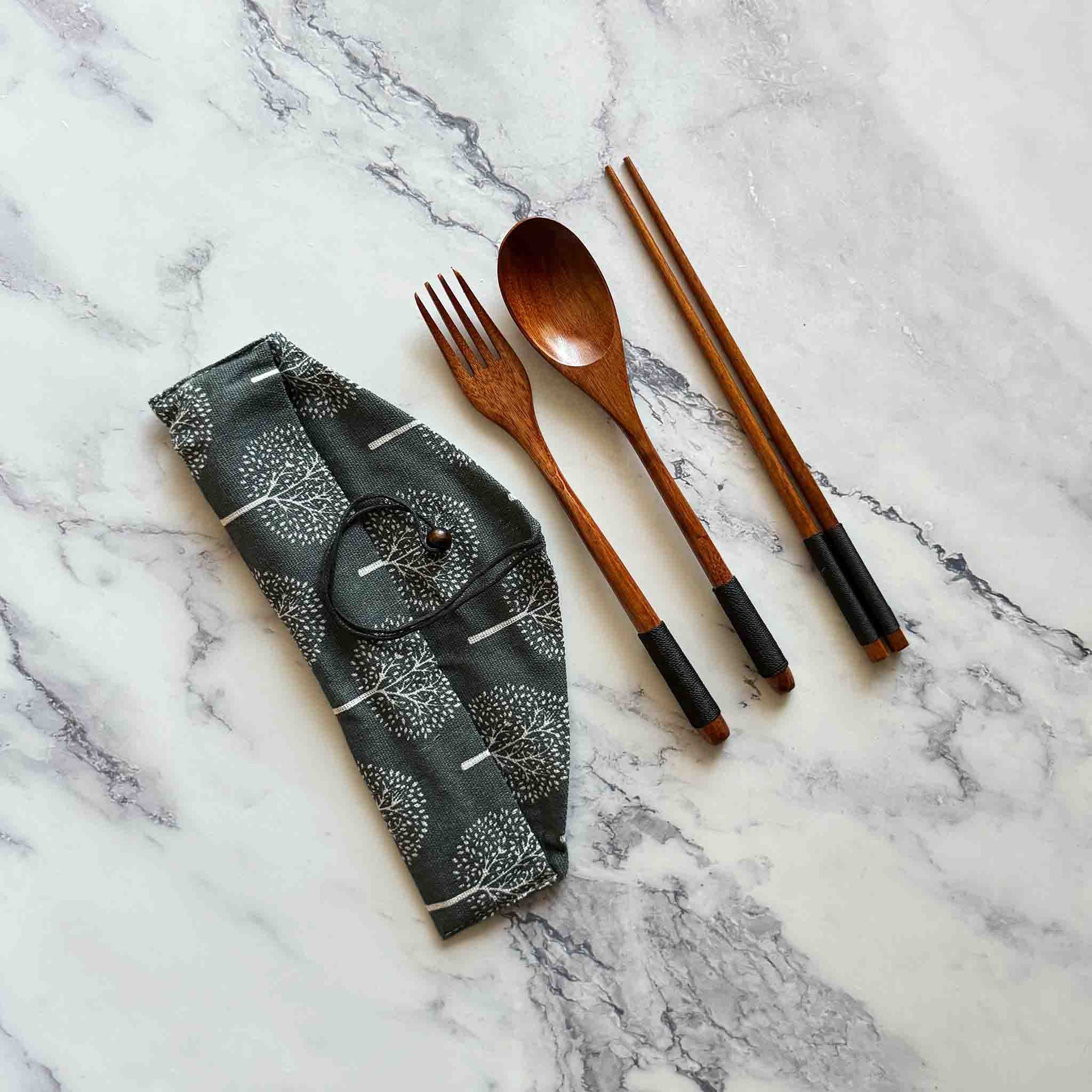 Coconut spoon, fork, and chopsticks next to cotton pouch on a marble surface