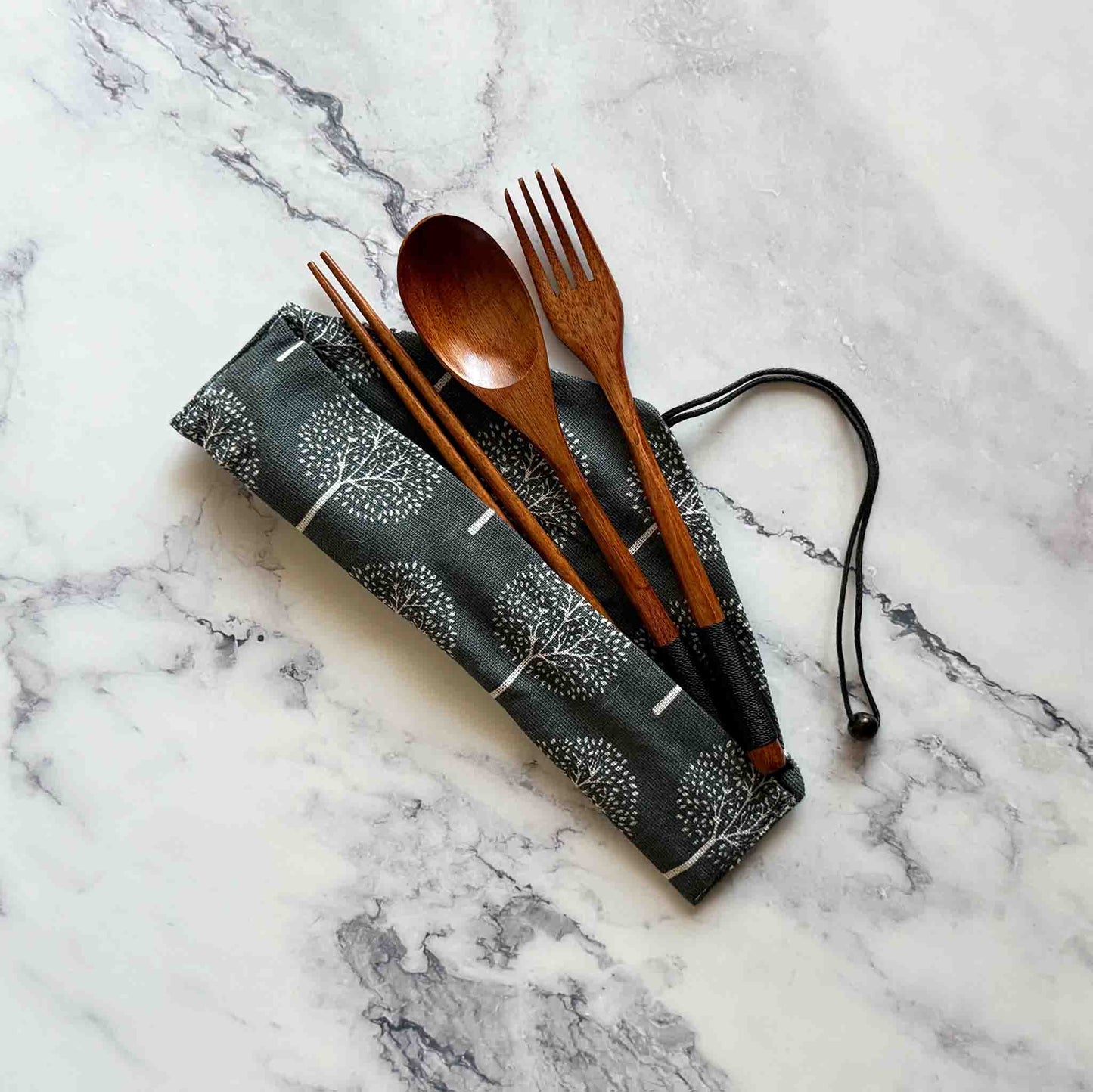 Coconut spoon, fork, and chopsticks next to cotton pouch on a marble surface