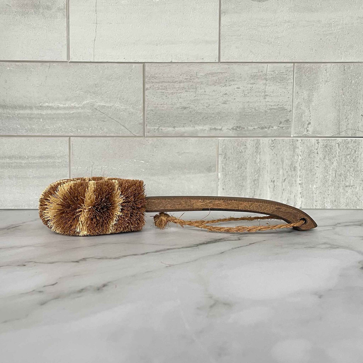 Brown brush with a wooden handle on a marble surface with a tiled wall background