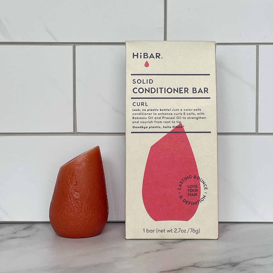 HiBAR Curl Solid conditioner bar and its packaging on a tiled bathroom wall background