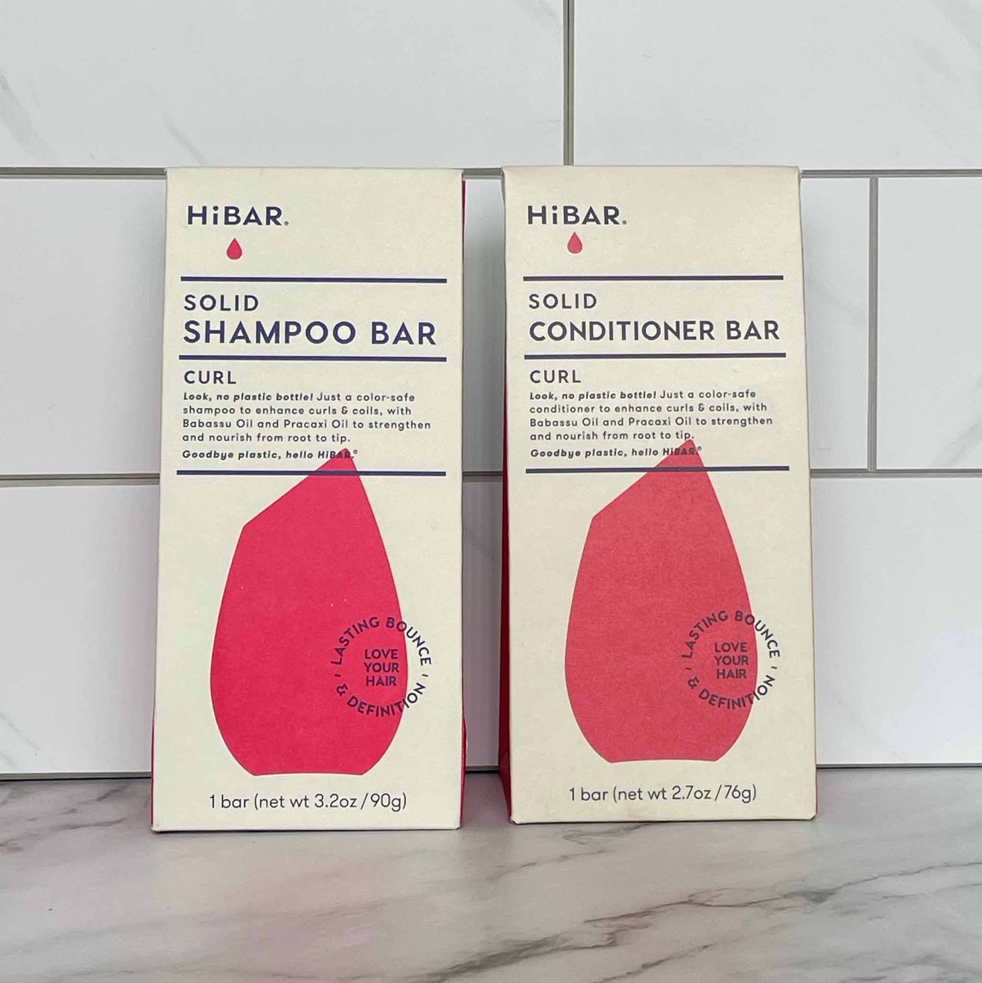 Two boxes of HIBAR Curl solid shampoo and conditioner bars on a tiled wall background