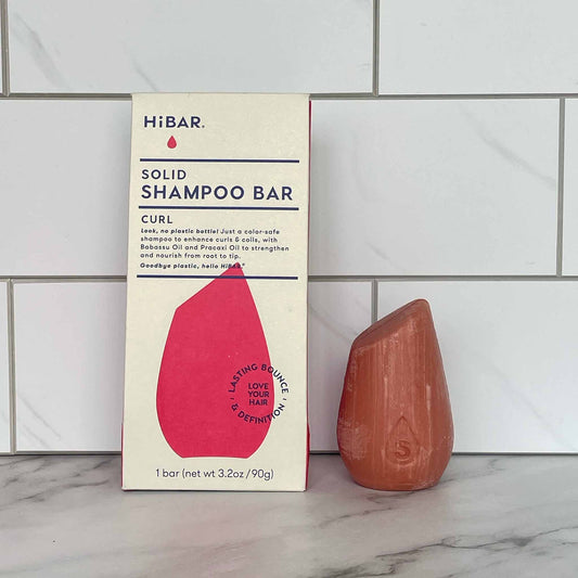 HiBAR Curl solid shampoo bar and its packaging on a tiled bathroom floor