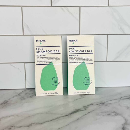 Two HIBAR solid Maintain shampoo and conditioner bars on a marble surface with tiled wall background