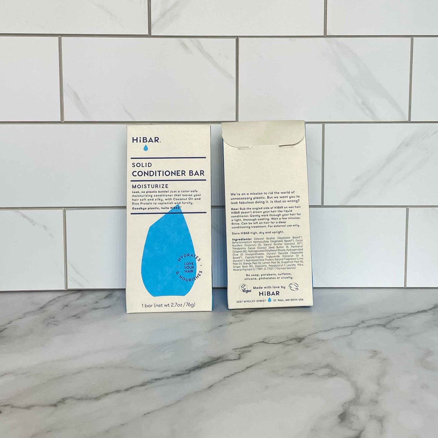 Two HiBAR Moisturize solid conditioner bar packages on a marble surface with tiled wall background