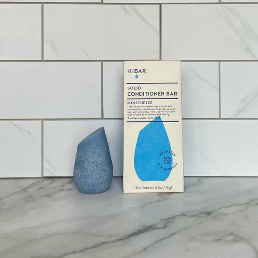 HiBAR Moisturize solid conditioner bar and its packaging on a marble surface with tiled wall background