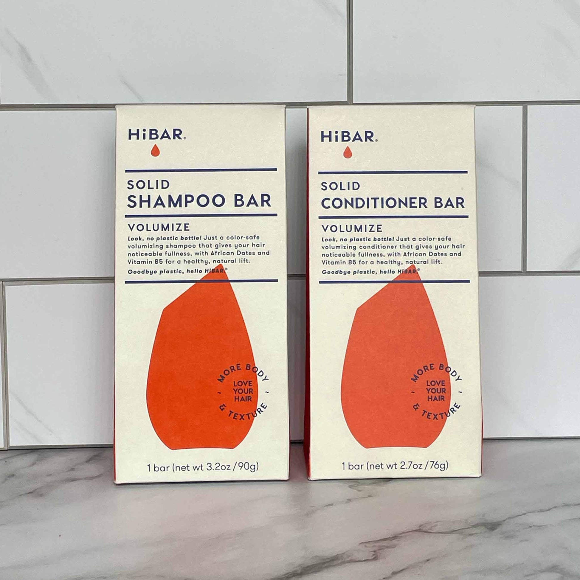 Two HiBAR Volumize solid shampoo and conditioner bar packages on a tiled wall background