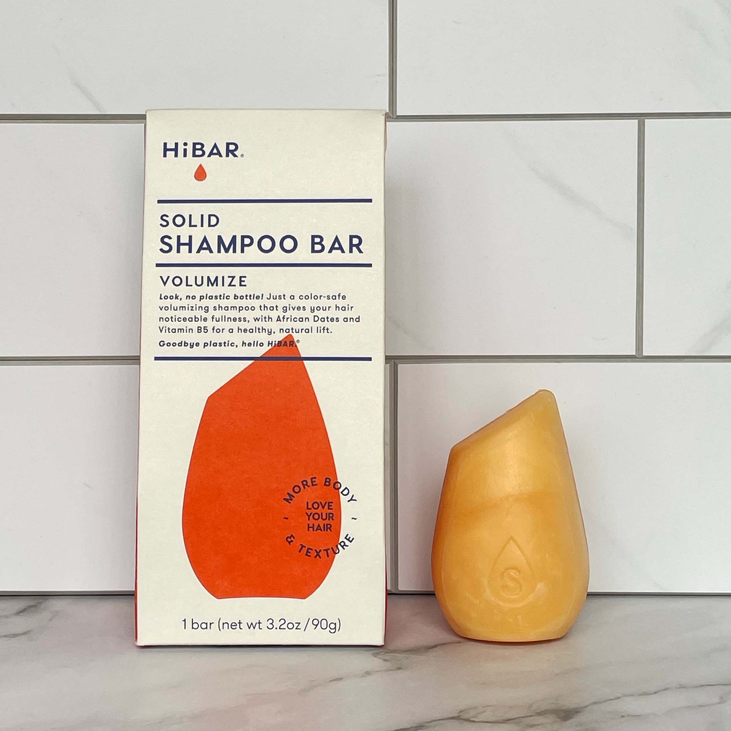 HiBAR Volumize Solid shampoo bar and its packaging on a tiled bathroom wall background