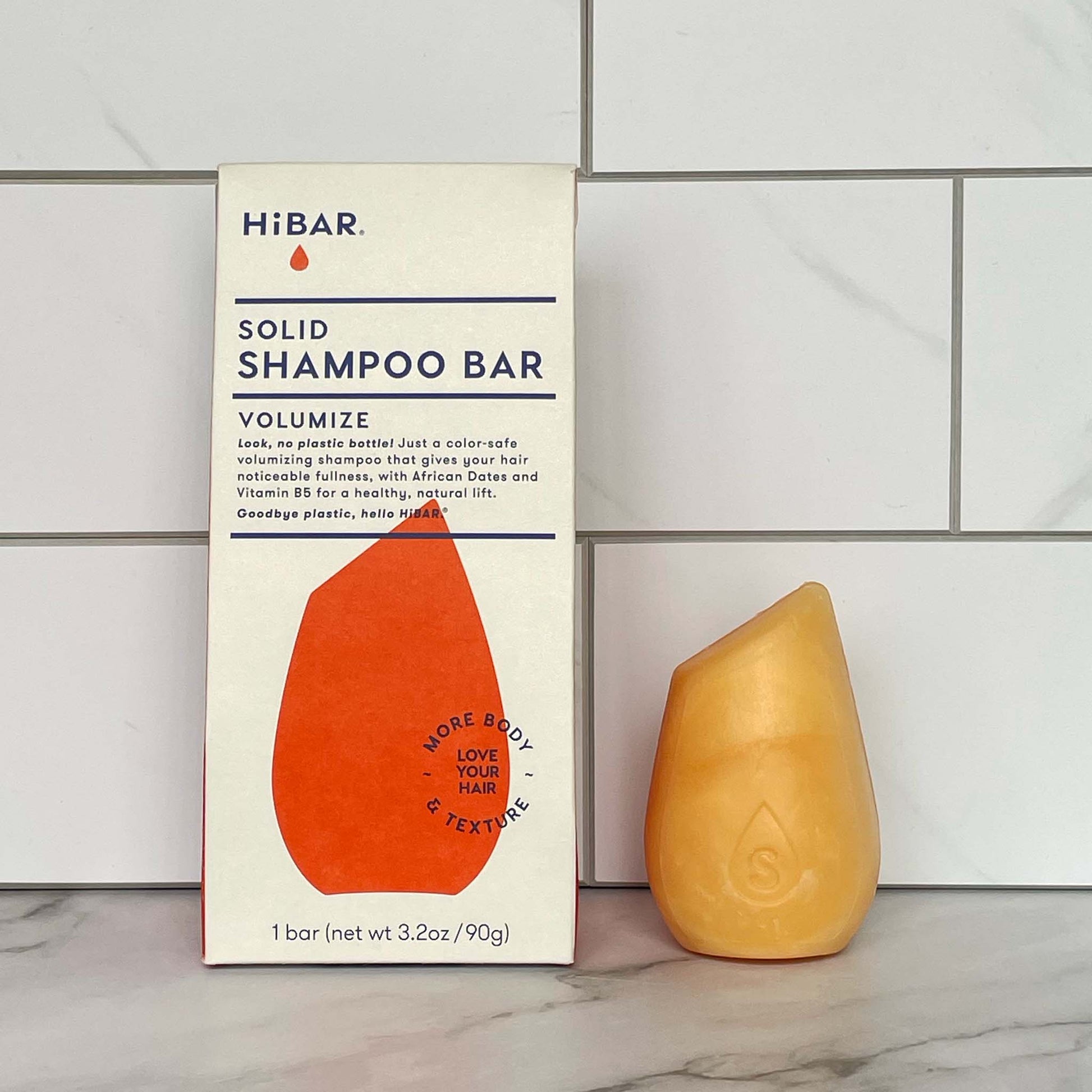 HiBAR Volumize Solid shampoo bar and its packaging on a tiled bathroom wall background