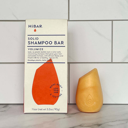 HiBAR Volumize Solid shampoo bar and its packaging on a tiled bathroom wall background