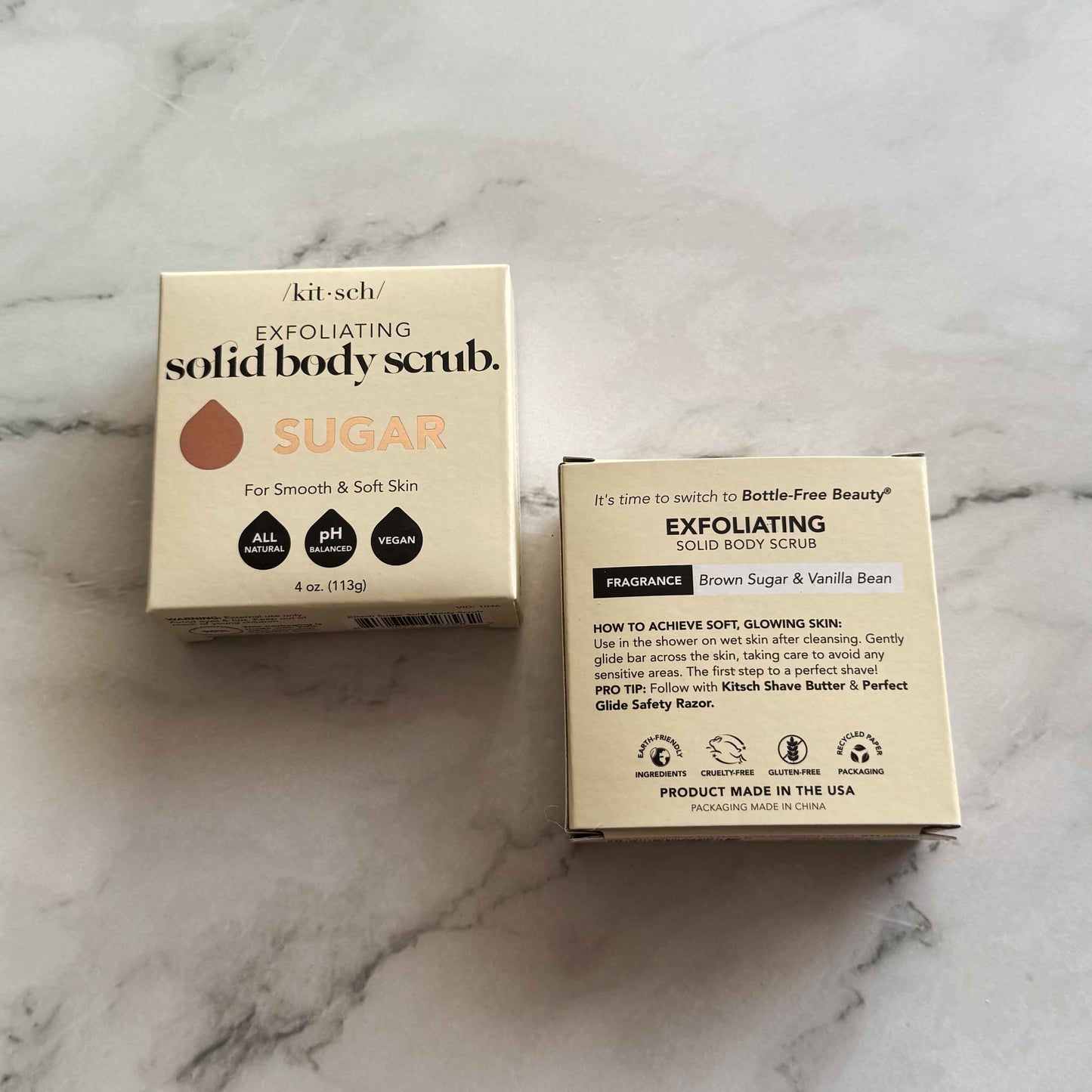 Two boxes of Kitsch solid body scrub bar on a marble surface