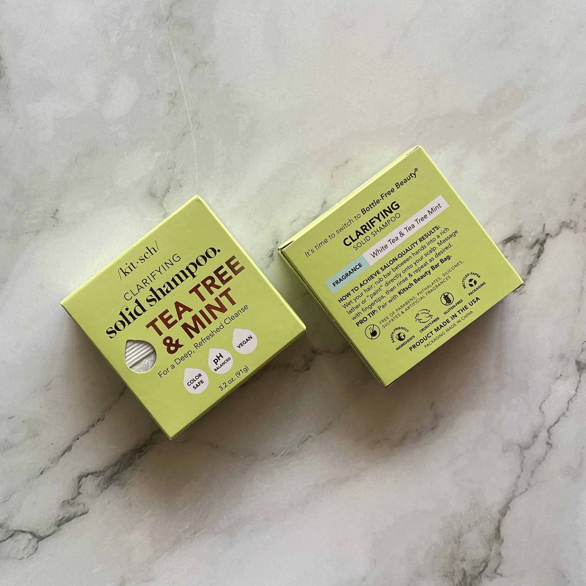 Two yellow boxes of Kitsch Tea Tree & Mint solid shampoo on a marble surface