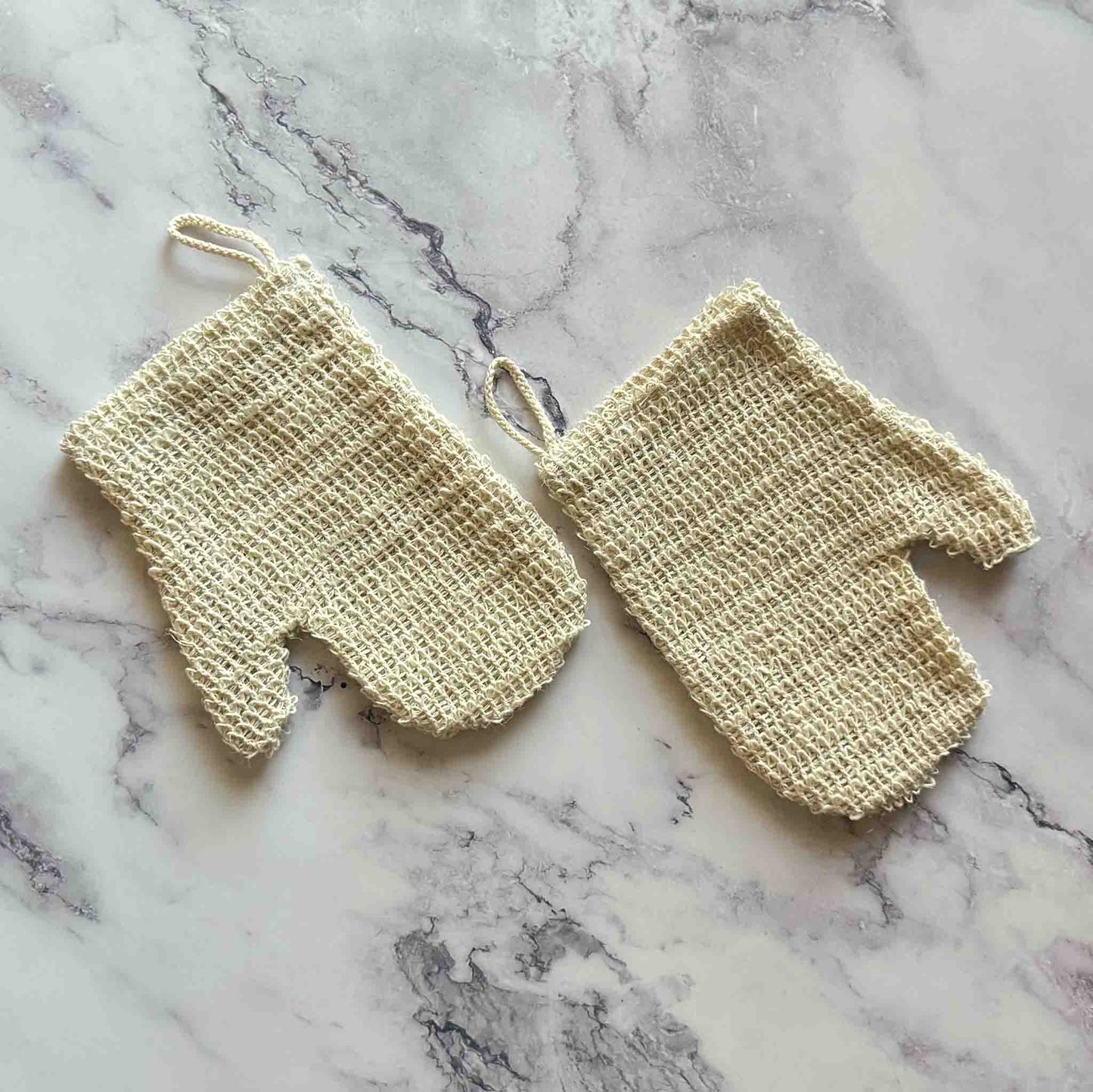 Pair of beige sisal exfoliating gloves on a marble surface