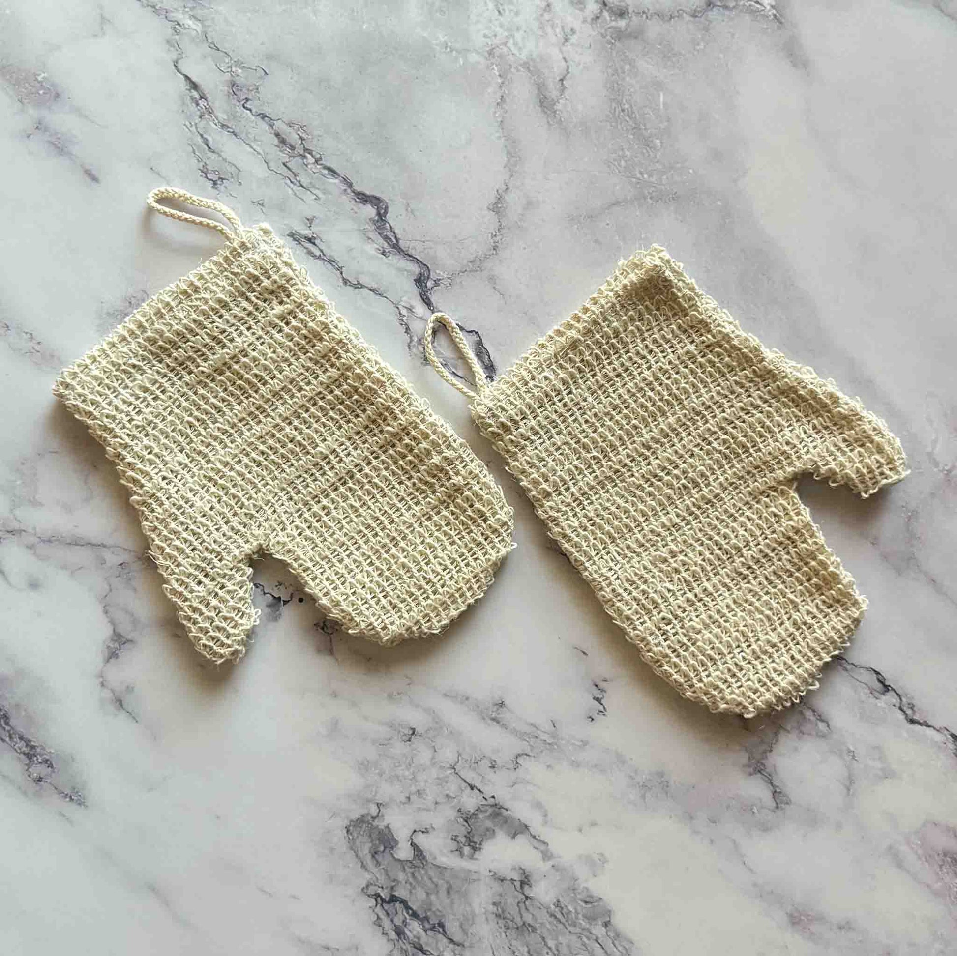 Pair of beige sisal exfoliating gloves on a marble surface