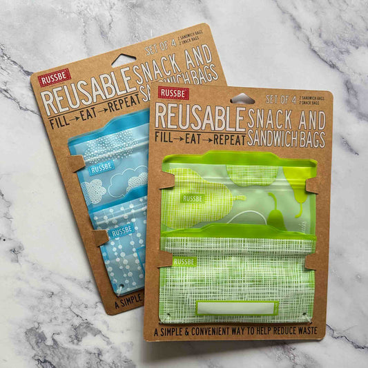 Two packages of Russbe reusable snack and sandwich bags on a marble surface.