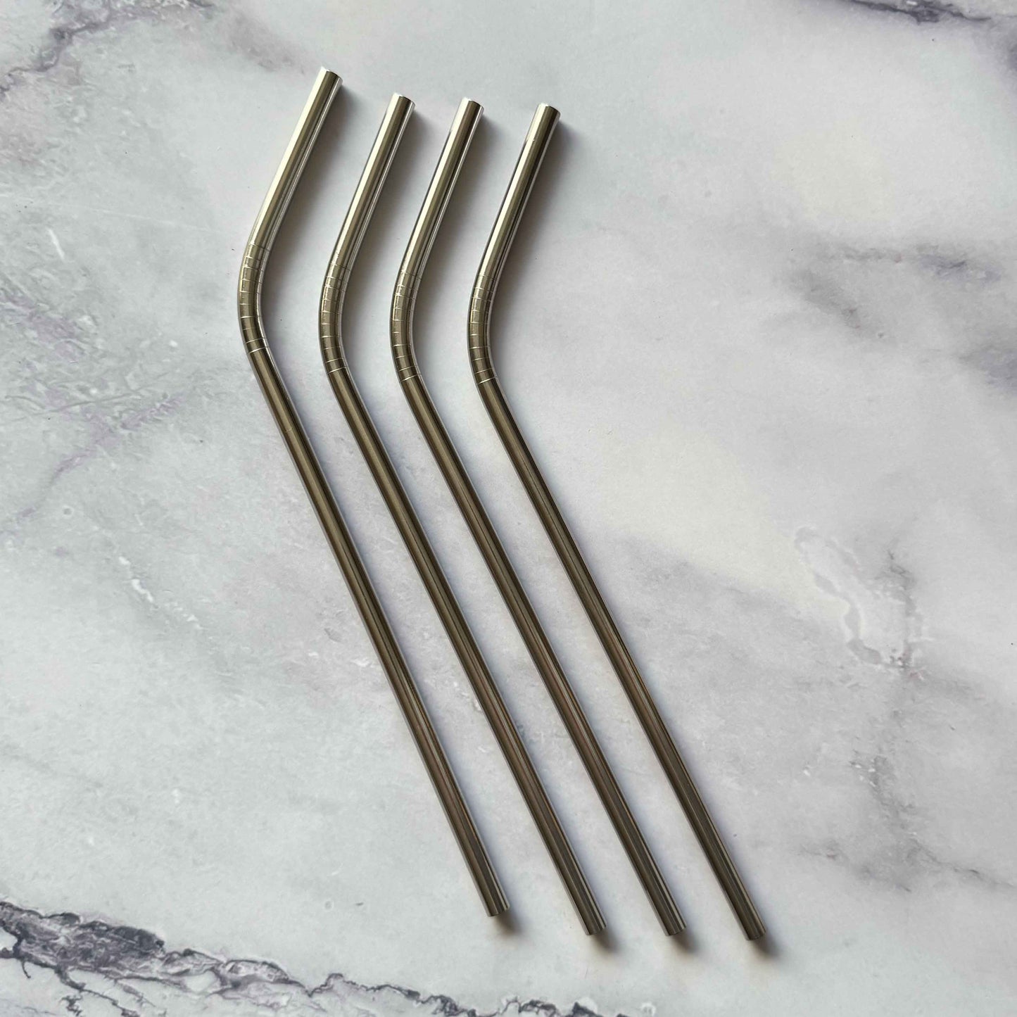 Four stainless steel bent straws on a marble surface